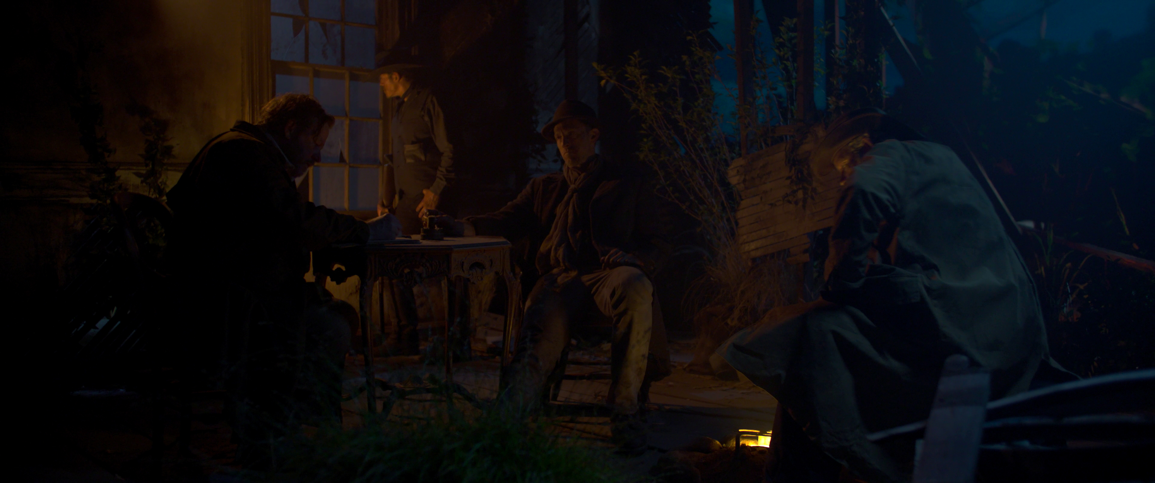 Nighttime scene from June July with costumed figures around a lantern-lit table